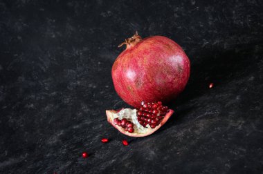 Juicy pomegranate fruit on a black-brown background with a piece with seeds. Side view. Daylight