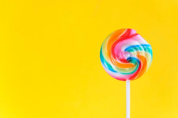 Colorful lollipop with colorful stripes on yellow background with copy space. Bright background for children's parties