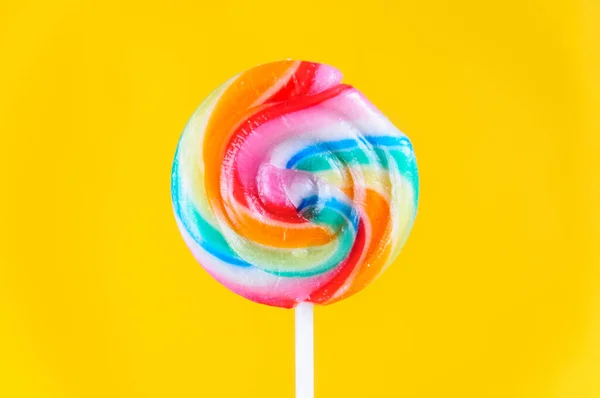 Round swirled candy on a stick of rainbow colors on a yellow background