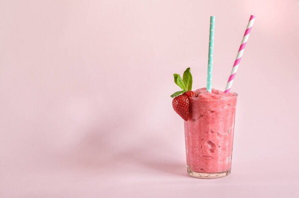 Strawberry smoothie in a glass with mint straws and strawberries on a pink background. Daylight with copy space for text  