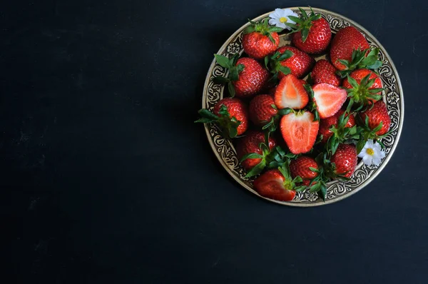 stock image Ripe strawberries in a beautiful plate on a black background. Daylight, selective focus with copy space