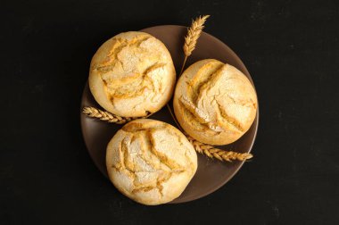 Kahverengi bir tabakta taze pişmiş yuvarlak çörekler. Siyah arkaplan, üst görünüm, doğal ışık, seçici odak