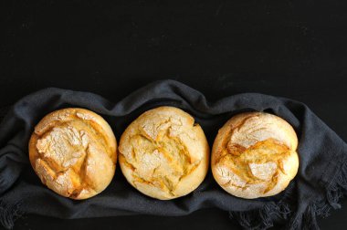 Siyah bir tahtanın üstünde siyah bir bezle üç çörek. Seçici odak, yukarıdan kopyalanan boşluklu doğal ışık