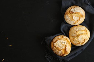 Siyah tahta arka planda üç taze çörek, koyu renk kumaş, üst manzara. Seçici odak, kopyalama alanı olan doğal ışık