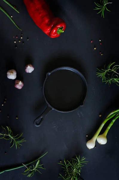 Frame of vegetables on a black vintage background with a cast iron skillet in the center. Natural light, selective focus, top view. vertical image