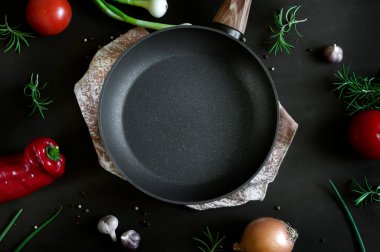 Ortada boş kızartma tavası, sebzeler, otlar ve siyah eski püskü bir arka planda baharatlar. Yukarıdan bak. Doğal ışıkta seçici odak