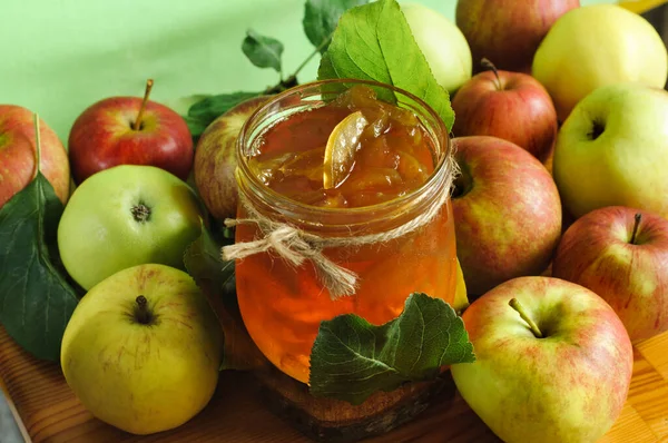 Apple jam in a transparent jar with apples and leaves on a wooden table. Selective focus in natural light. View from a high angle