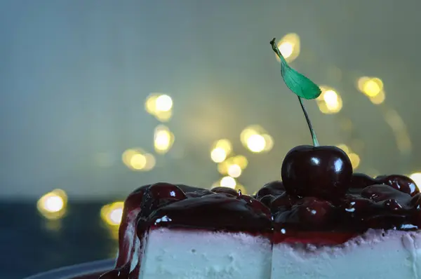 A piece of cream cake with cherries close-up in a cafe in the evening light. Selective focus, bokeh