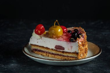 Siyah arka plandaki bir tabakta renkli meyveli pasta, ön manzara, doğal ışık. Seçici odak