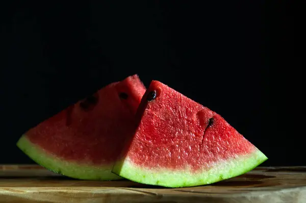 İki porsiyonlu taze karpuz parçası ve siyah arka planda tohumlar.