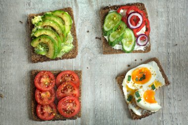 Dört lezzetli sandviç, tam tahıllı çavdar ekmeği, yumurta ve çeşitli sebzeler ve baharatlar. Üst görünüm