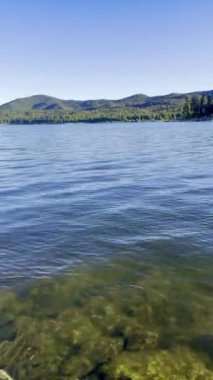 Video, kıyıya vuran yumuşak göl dalgalarını yakalar, rahatlatıcı, ritmik bir ses yaratır. Işıl ışıl su güneşin altında parlıyor. Huzurlu ve huzurlu bir ortam yaratıyor.