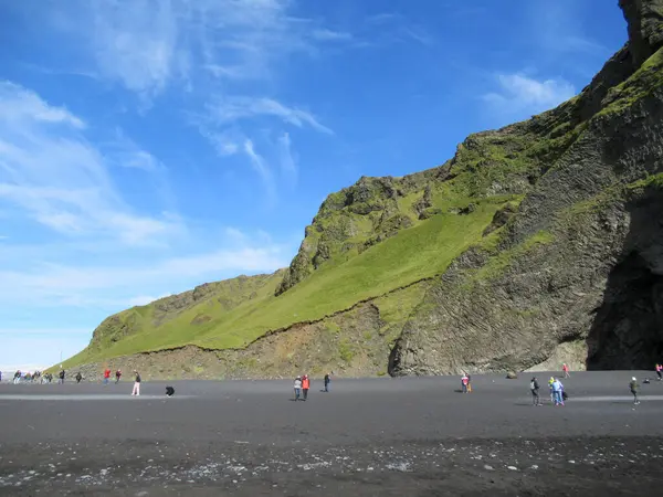 Grass covered cliffs at Reynisfjara beach in Iceland with blue sky and white cloud formations