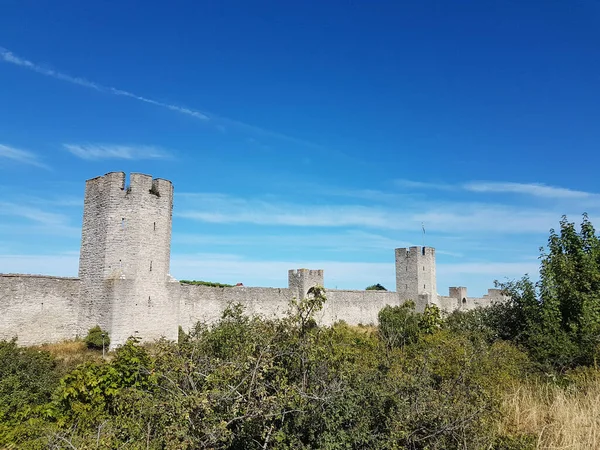 Medieval stone wall and towers, green trees and bushes and blue sky in Visby, Sweden