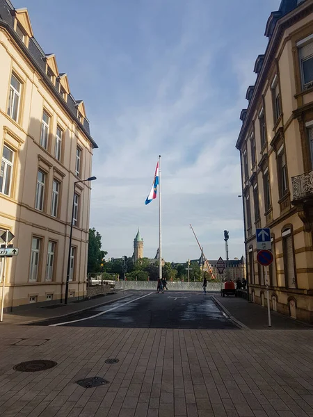 Tall flagpole with large Luxembourg flag seen between fancy buildings