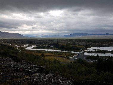 River, houses and parking lot with mountains on the background on a cloudy day at Thingvellir National Park in Iceland