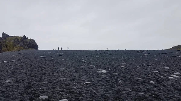 People at a black sand beach in Iceland from low angle against grey sky