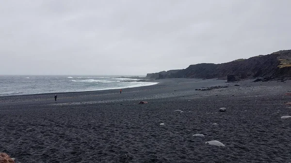 People at Djupalonssandur beach in Iceland with black sand, rocks and ocean waves