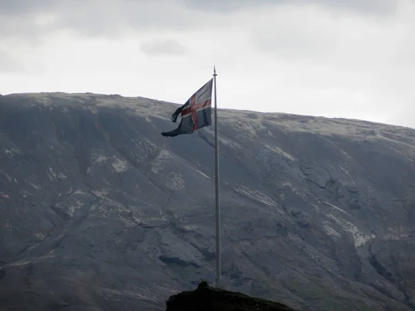 Icelandic flag on a flagpole against a rugged mountain