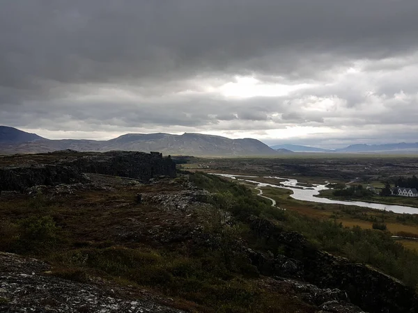 River, houses and parking lot with mountains on the background on a cloudy day at Thingvellir National Park in Iceland