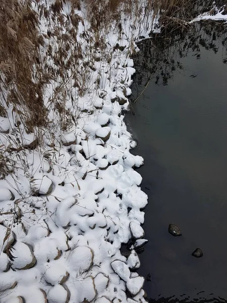 Dark water lined with snow-covered round stones