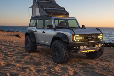  Ford Bronco Raptor vahşi arazide, keşif ekipmanları ve bir çatı çadırıyla donatılmış.