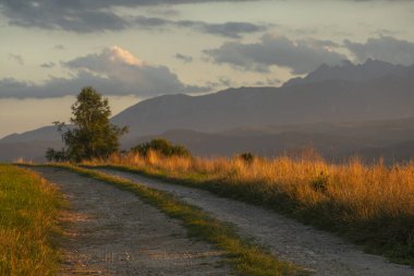 Gün batımında arka planda dağlar olan çakıl yolu.