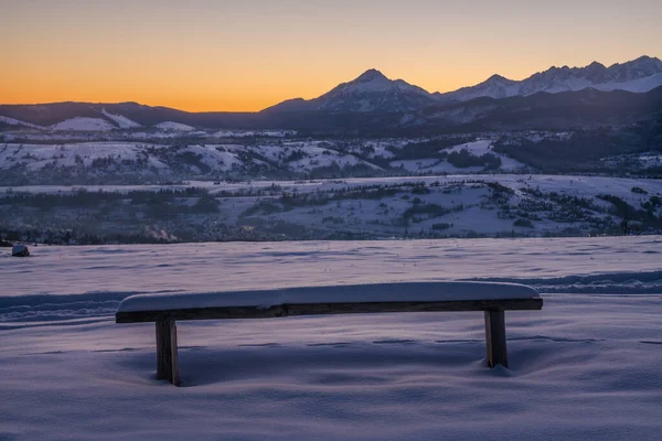 Wooden bench covered in snow with a view of snow-capped mountain peaks on a frosty morning