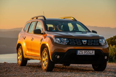 Dacia Duster SUV arka planda dağlar olan çakıllı bir otoparkta..
