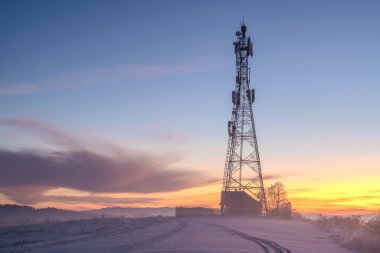 Soğuk bir sabahta bir dağın tepesinde cep telefonu telekomünikasyon direği.