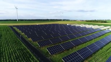 Güneş Çiftliği inşaatı. Güneş enerjisi panelleri, fotovoltaik ve rüzgar türbinlerinin hava görüntüsü. Güneş enerjisi santrali yapım aşamasında, mısır tarlası ve rüzgâr tarlası yakınlarında. Sürdürülebilir kaynaklar ve alternatif elektrik kaynağı kavramı.