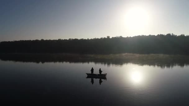 湖の真ん中にある漁船で2人の釣り人の空中シルエットビュー 日の出に釣る2人の漁師 — ストック動画