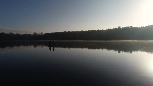 湖の真ん中にある漁船で2人の釣り人の空中シルエットビュー 日の出に釣る2人の漁師 — ストック動画