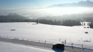 Dağ yolu kışın karla kaplı ve at arabası, hava manzaralı. Efsanevi, karlı beyaz kış ve karlı dağ sıraları. Destansı Alp manzaralı ve araba süren bir yol. Kış yolculuğu.