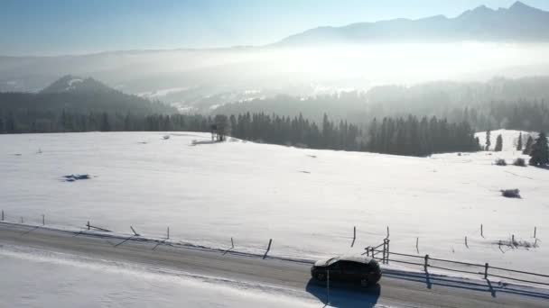 冬の雪と乗用車 空中視界で覆われた山道 エピック 雪の白い冬 雪が山の範囲を捉えました 壮大なアルペンビューと車の運転による道 ウィンターロードトリップ — ストック動画
