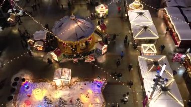 Kış gecesi hava manzaralı Noel pazarında. Bayram atlıkarıncaları, buz pateni pisti, büyük süslü bir ağaç ve dönme dolap. Modern bir şehirde aydınlatılmış Tatil Fuarı.