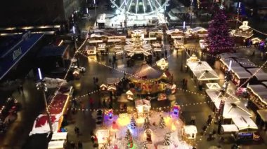 Kış gecesi hava manzaralı Noel pazarında. Bayram atlıkarıncaları, buz pateni pisti, büyük süslü bir ağaç ve dönme dolap. Modern bir şehirde aydınlatılmış Tatil Fuarı.