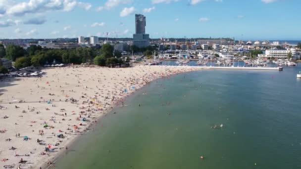 近代的な海辺の都市グディニアのビーチ 空気の眺め ヨット港とマリーナ近くの混雑したビーチのショットを確立 晴れた夏の日にバルト海で日光浴 — ストック動画