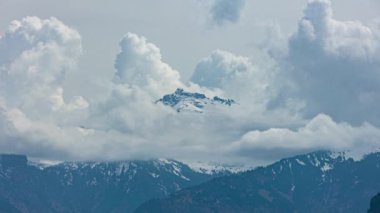 Zaman kaybı, dağların tepesinde karla kaplı dans eden bulutlar. Kanton Glarus, İsviçre.