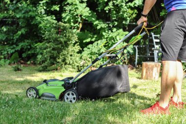 Çim biçme makinesi arka bahçede yeşil çim biçer, çimleri biçer. Arka bahçesindeki çimleri biçme makinesiyle kesen bir adam..