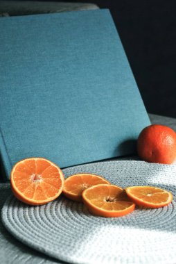 Gri yüzeyine oymalı kitap ve taze dilimlenmiş portakal. Portakal meyveli model tasarım. Bir mavi kitap düzeni.
