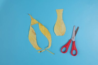 Adım adım çocuklar için sonbahar doğa zanaatı, bırakın ve makas mavi arka planda, üst görünüm