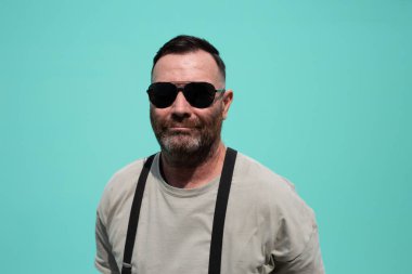 Güneş gözlüğü takan sakallı adam, yakın plan portre, yaz titreşimleri, gök mavisi arka plan.