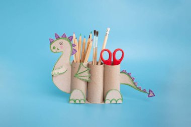 ejderha şekli bir kalem tutacağı tuvalet kağıdı ve bir makas, geri dönüşüm konsepti, çocuklar için DIY, basit aktivite, mavi arka plan