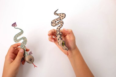 Geri dönüşümlü kağıttan yapılmış bir parmak yılanı ya da ejderha zanaatı, DIY, eğitim sanatı ve çocuklar için el işi, üst görünüm, üzerinde yılan olan bir kağıt parçası tutan kişi, sevimli bir oyuncak., 