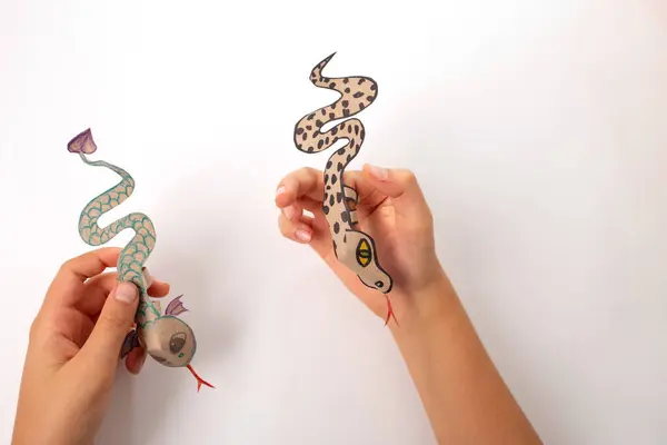 a finger snake or dragon craft made out of recycled paper, DIY, tutorial, educational art and craft for kids, top view, a person holding a piece of paper with a snake on it, cute toy,
