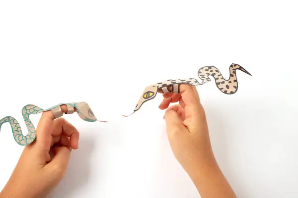 Geri dönüşümlü kağıttan yapılmış bir parmak yılanı veya ejderha zanaatı, DIY, çocuklar için eğitici sanat ve zanaat, üst görünüm, kağıt yılanı tutan bir kişinin yakın çekimi, bir çocuk çizimi., 