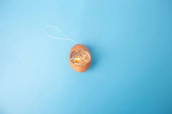 close up of a broken egg shell craft with nest inside, sitting on top of a blue surface, Easter home decor craft concept,