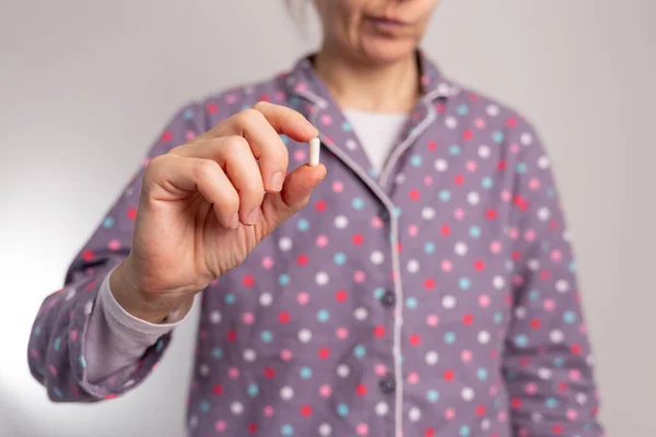 a woman holding a pill in her hand, soft focus, front view, wearing pajamas, closeup photo, half body photo,