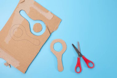 Mavi yüzey üzerinde oturan bir makas, kartondan kesilmiş, büyüteç şekli, özel ders, basit zanaat fikirleri, DIY, okul projesi, geri dönüşüm